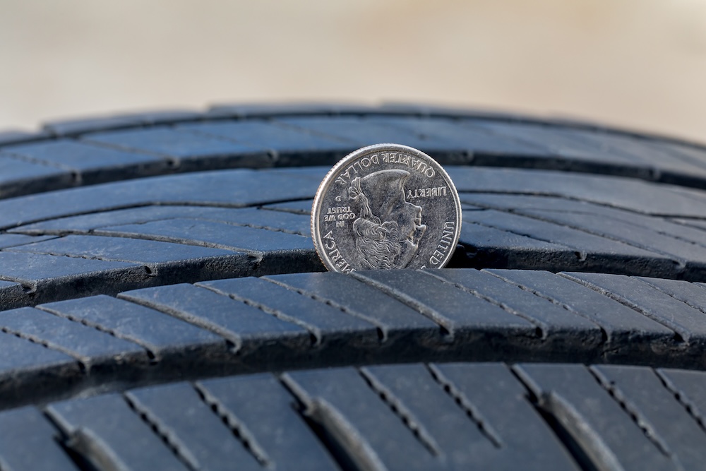 Closeup of checking tire tread wear depth of old tire using a quarter coin Concept of automobile safety maintenance and repair