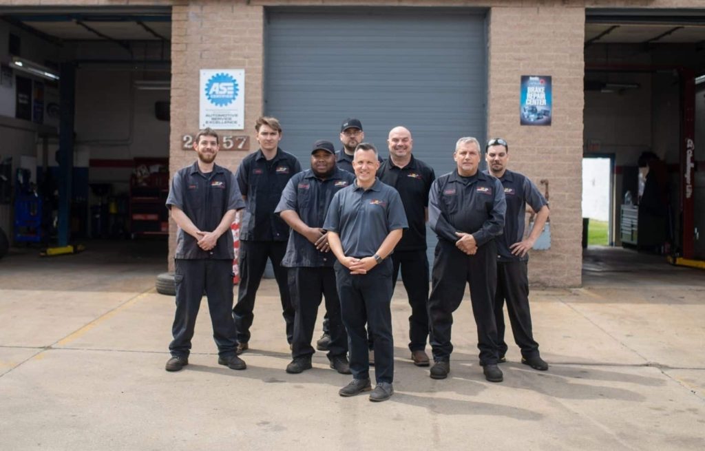 Group of automotive technicians posing in front of a repair shop with a closed garage door.