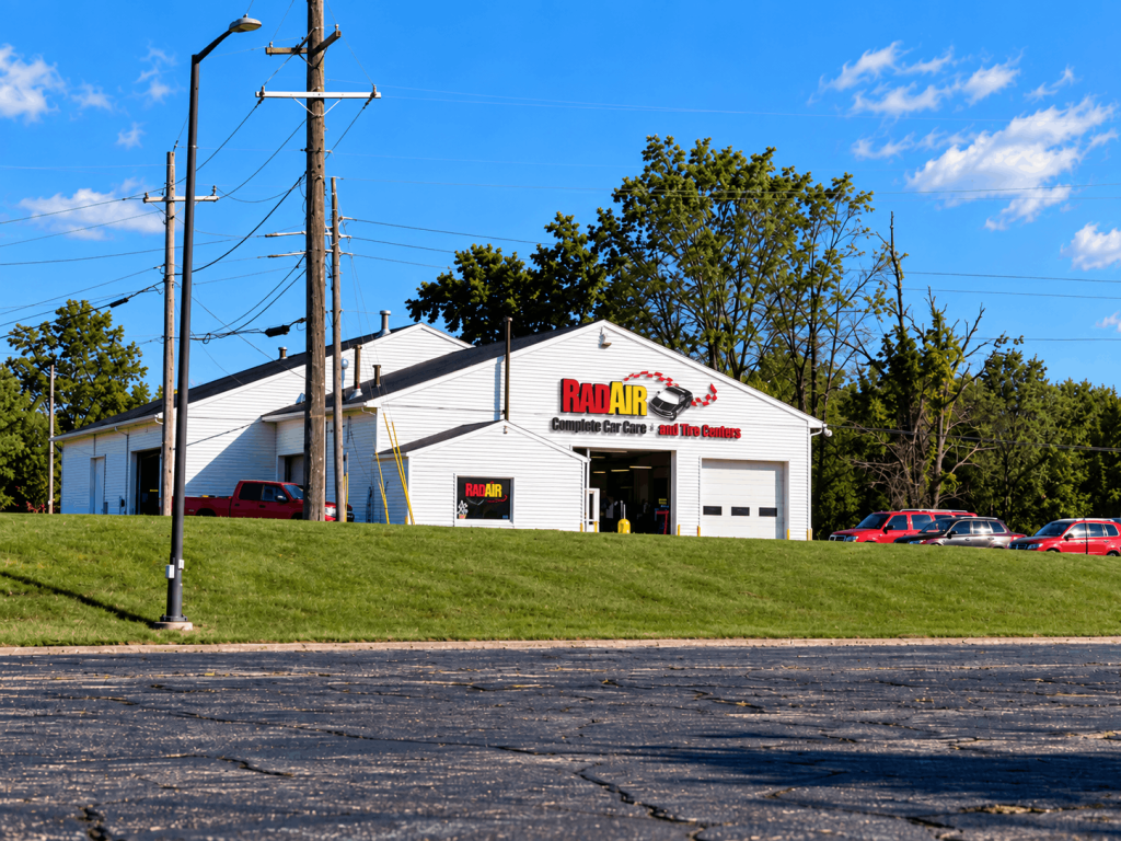 Auto repair shop building with 'RAD AIR' sign and several cars in the parking lot on a sunny day, power lines in the foreground.